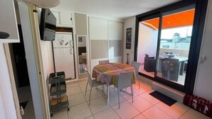 A compact living space with a dining area, kitchenette, and a sliding glass door to an outdoor terrace.