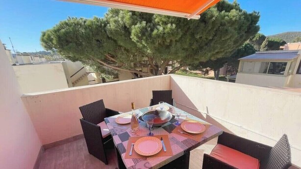 A balcony with a table set for dining, surrounded by wicker chairs, and a large tree in the background.