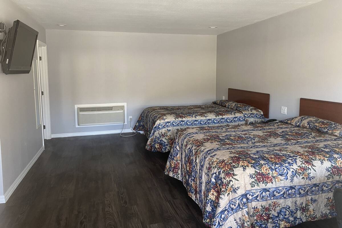 A hotel room with two beds, a flat-screen TV mounted on the wall, and a window with a closed blind.