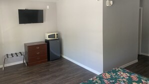Ein Schlafzimmer mit Bett, Kommode, Mikrowelle, Fernseher und einer Tür zu einem weiteren Raum.