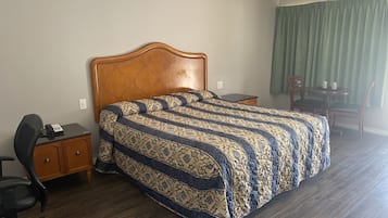 Une chambre d’hôtel avec un grand lit, un bureau, une chaise et une petite table. Un rideau vert est visible en arrière-plan.
