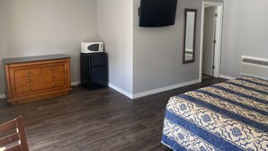 Ein Schlafzimmer mit Bett, Kommode, Mikrowelle, Fernseher und einer Tür zu einem weiteren Raum.