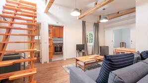 Uma sala de estar moderna com escada de madeira, sofá cinzento e área de refeições com mesa e cadeiras.