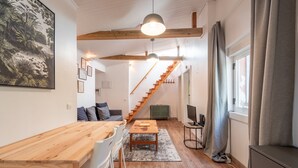 Um espaço de estar moderno com mesa de jantar de madeira, sofá, escada e uma janela grande com cortinas.