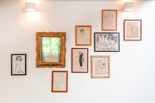 Una pared galería con diversas obras de arte enmarcadas y un espejo grande y ornamentado.