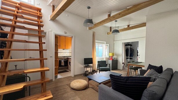 Um interior moderno com escada estilo loft, um sofá cinzento e uma cozinha ao fundo.