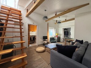 A modern interior with a loft-style staircase, a grey sofa, and a kitchen in the background.