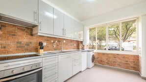 A kitchen with white cabinets, a brick backsplash, a window with a view of the outside, and a built-in oven. - GuestReady - Great 3BDR apartment in Oeiras! (Oeiras)