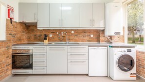 A modern kitchen with white cabinets, a brick backsplash, a stainless steel oven, a dishwasher, and a washing machine. - GuestReady - Great 3BDR apartment in Oeiras! (Oeiras)