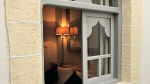 A window with a white frame and a view into a room with a lamp and a bed.