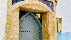 A building entrance with a decorative archway, a metal door with a handle, and a small window above the door.