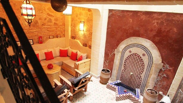 A cozy room with a stone wall, a wooden sofa with red cushions, a small table, and a tiled floor.