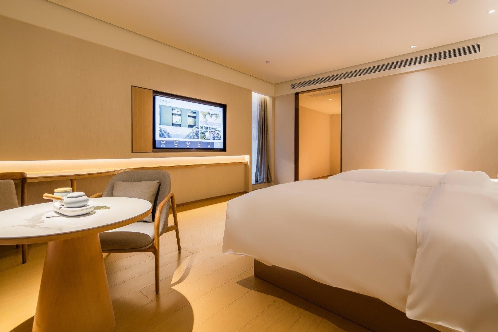 Una habitación de hotel con una cama, un escritorio con silla, un televisor montado en la pared y una ventana con cortinas.