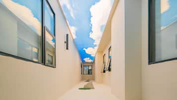 A narrow hallway with a ceiling painted to resemble a sky with clouds, large windows on both sides, and a small rug on the floor.