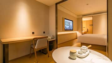 A hotel room with a bed, a desk, a chair, a table with a tea set, and a television mounted on the wall.