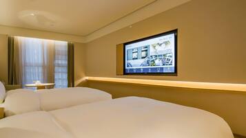 A hotel room with two beds, a television mounted on the wall, and a window with curtains.