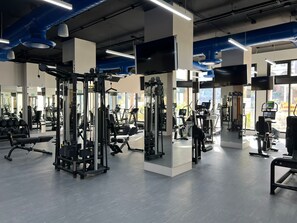 Une salle de sport équipée de divers appareils d’exercice, dotée de grandes fenêtres et d’un design moderne.