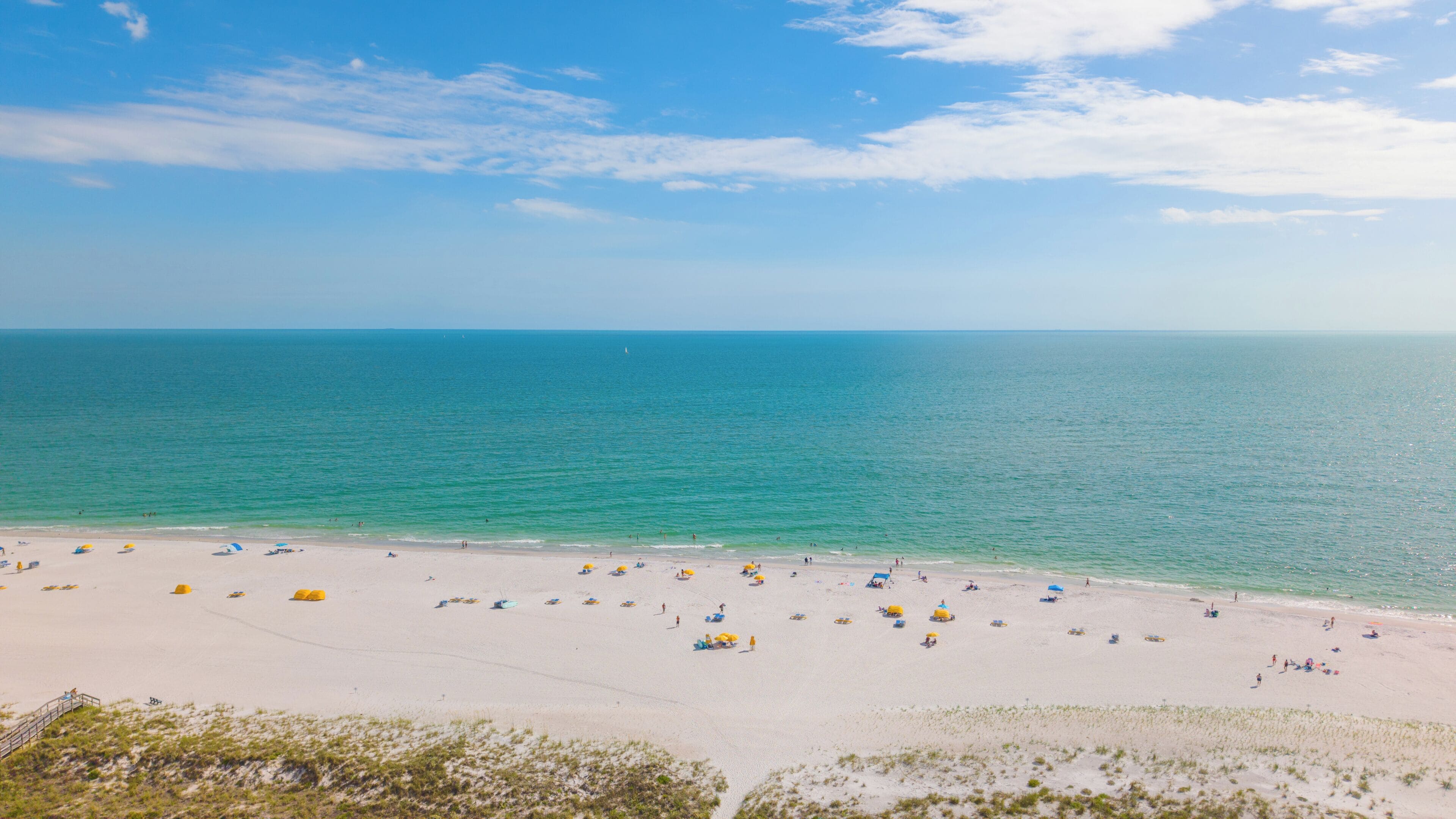 A beach with numerous umbrellas and people, a clear sky, and calm sea.
