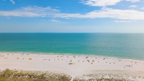 A beach with numerous umbrellas and people, a clear sky, and calm sea.