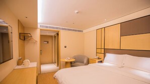 Habitación de hotel con una cama grande, una mesita de noche con lámpara, una silla, una pequeña mesa redonda y un espejo.