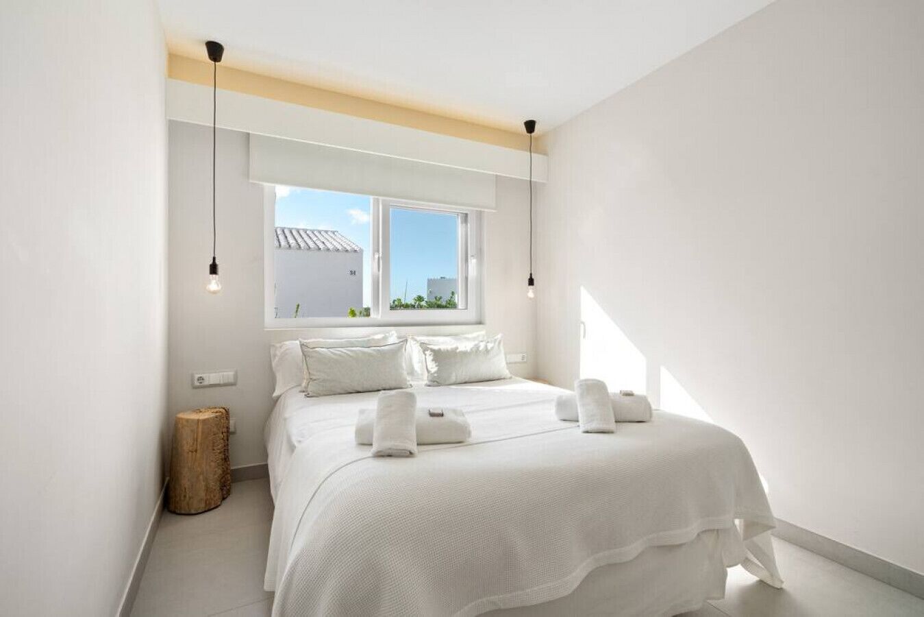 A bedroom with a large bed, two bedside tables, a window with a view, and a wooden stool.