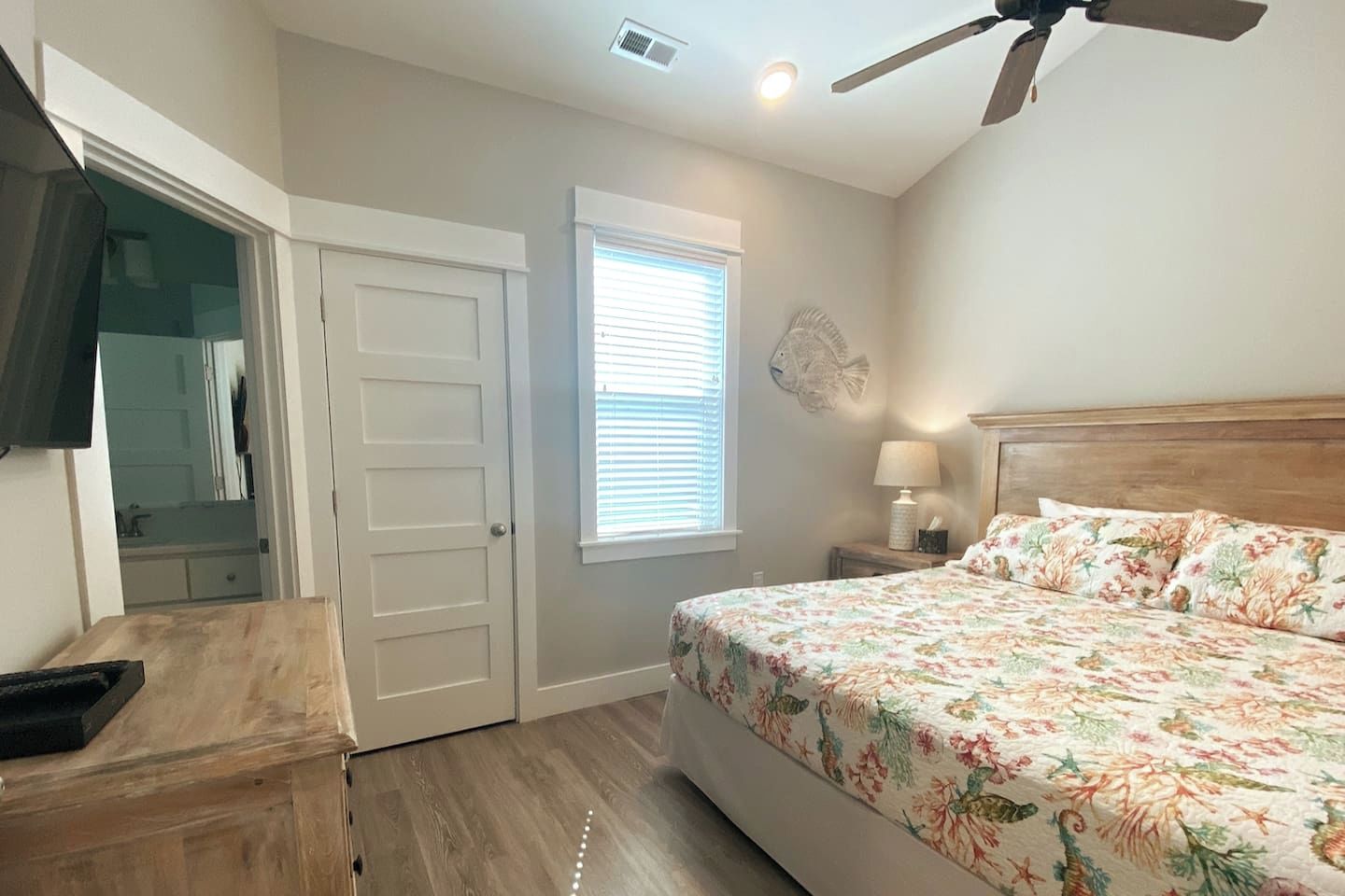 A bedroom with a bed, a ceiling fan, a window with blinds, and a door leading to a bathroom.