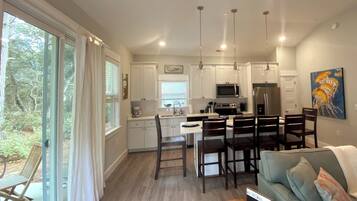 A modern kitchen with white cabinets, a dining area with wooden chairs, and a large window with curtains.
