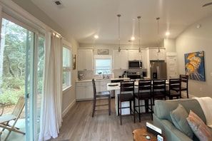 A modern kitchen with white cabinets, a dining area with wooden chairs, and a large window with curtains.
