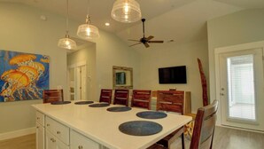 A dining area with a large island, wooden chairs, pendant lights, a ceiling fan, and artwork on the walls. - Dog Friendly Luxury Condo, Walk to the Beach (Corolla)