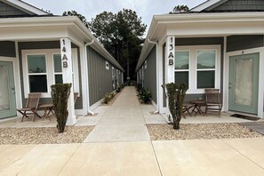A row of two-story buildings with numbered doors, a paved walkway, and outdoor seating. - Dog Friendly Luxury Condo, Walk to the Beach (Corolla)