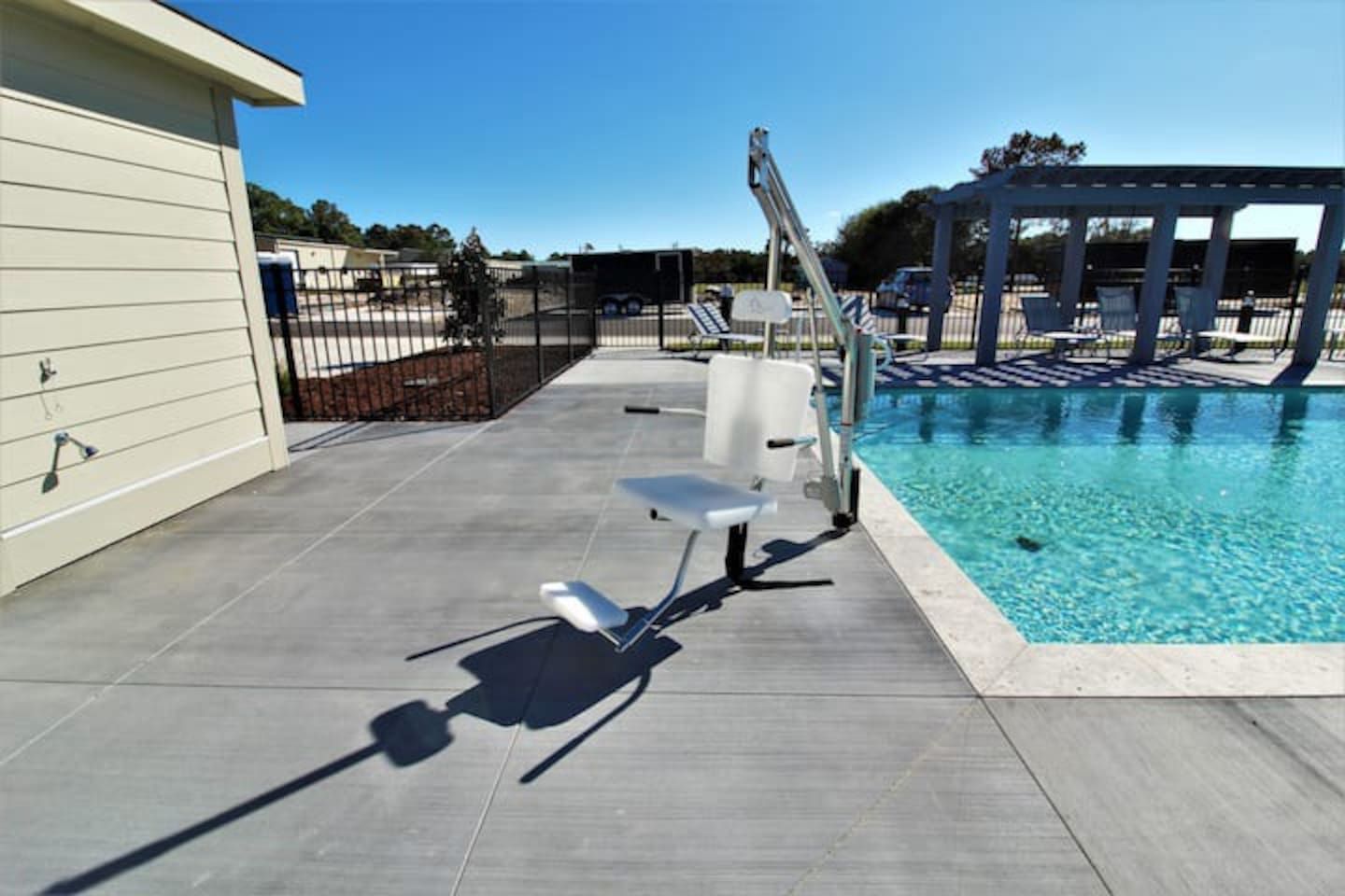 A swimming pool area with a sun lounger, a pergola, and a fenced patio.