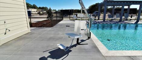 A swimming pool area with a sun lounger, a pergola, and a fenced patio.