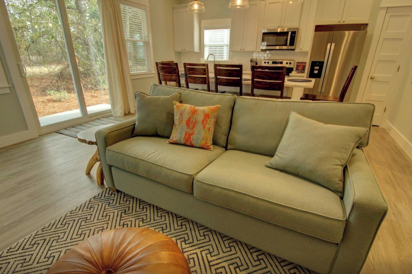 A modern living room with a sofa, a patterned rug, and a dining area with chairs.