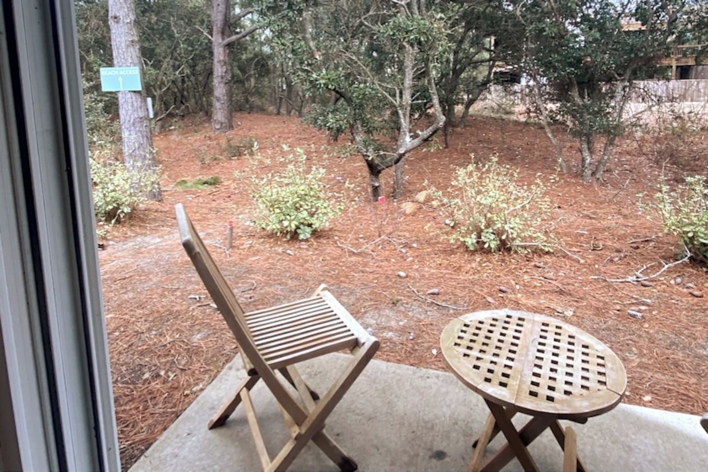 A patio area with a wooden chair and table, surrounded by trees and a sign indicating a search area.