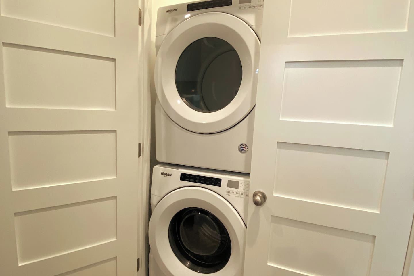 A set of stacked Whirlpool washing machines in a white door closet.
