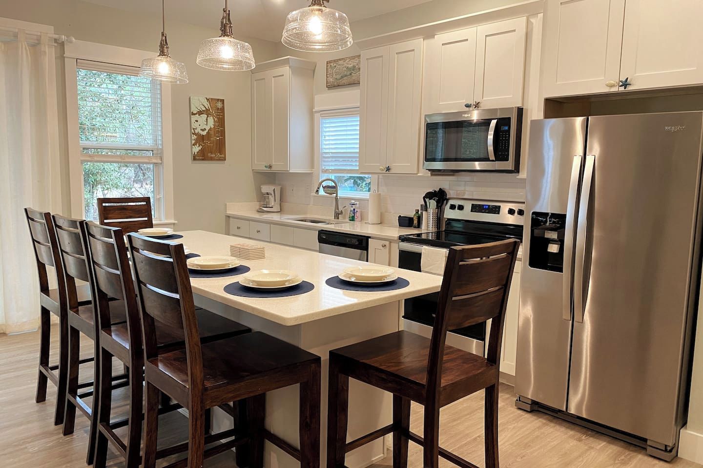 A modern kitchen with white cabinets, a stainless steel refrigerator, a microwave, and a dining table with chairs.