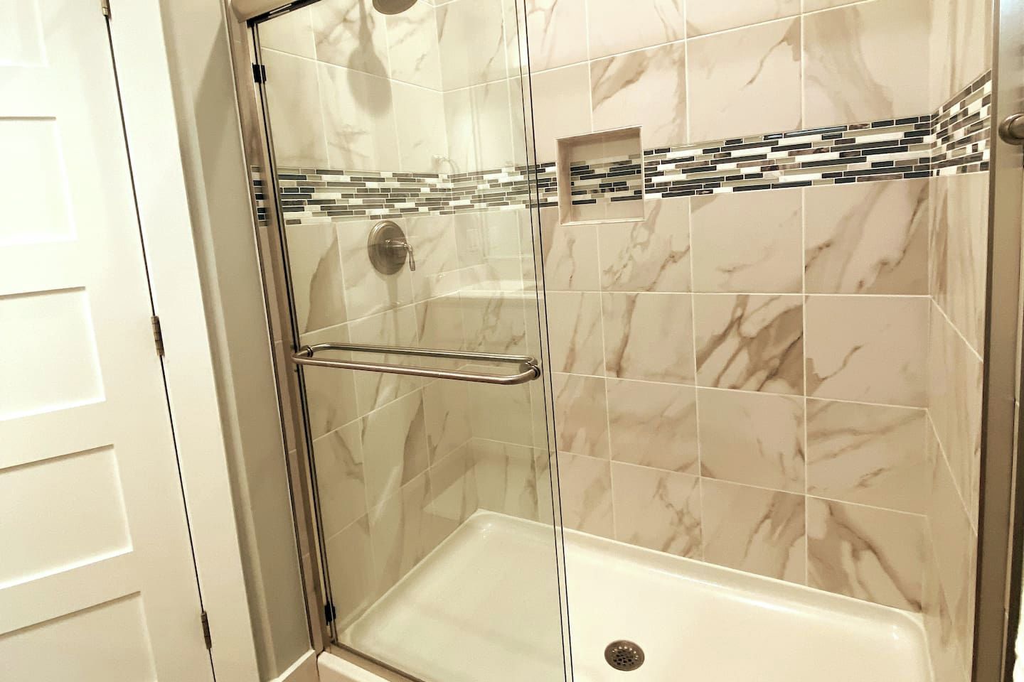 En dusch med glasväggar, ett vitt badkar, marmorplattor och en metallhanddukshängare.