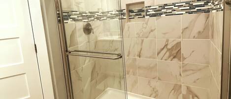 A glass-enclosed shower with a white bathtub, marble tiles, and a metal towel rack.