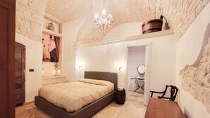 Quarto com parede de pedra, cama, baú de madeira e um candelabro.
