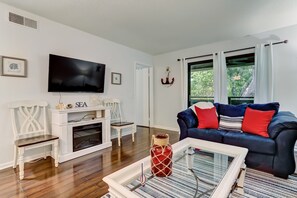 A living room with a TV, white entertainment unit, blue sofa, and a glass coffee table. - Short walk to the beach- 2BR, 2BA “Tranquility on Amelia" (Fernandina Beach)