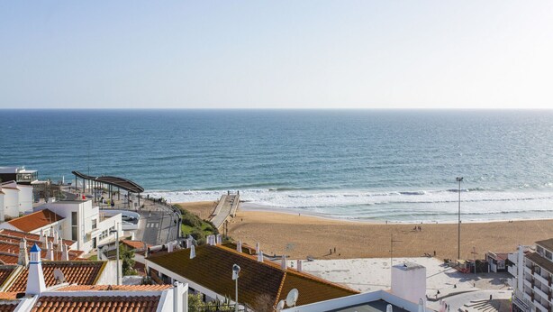 Vista costera con playa, paseo marítimo y edificios con techos de tejas rojas.