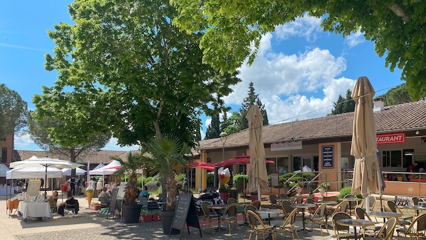 An outdoor café area with tables and chairs, surrounded by trees and umbrellas. - Holiday home - 1-6 person(s) - quiet location - large fenced property (Méjannes-le-Clap)