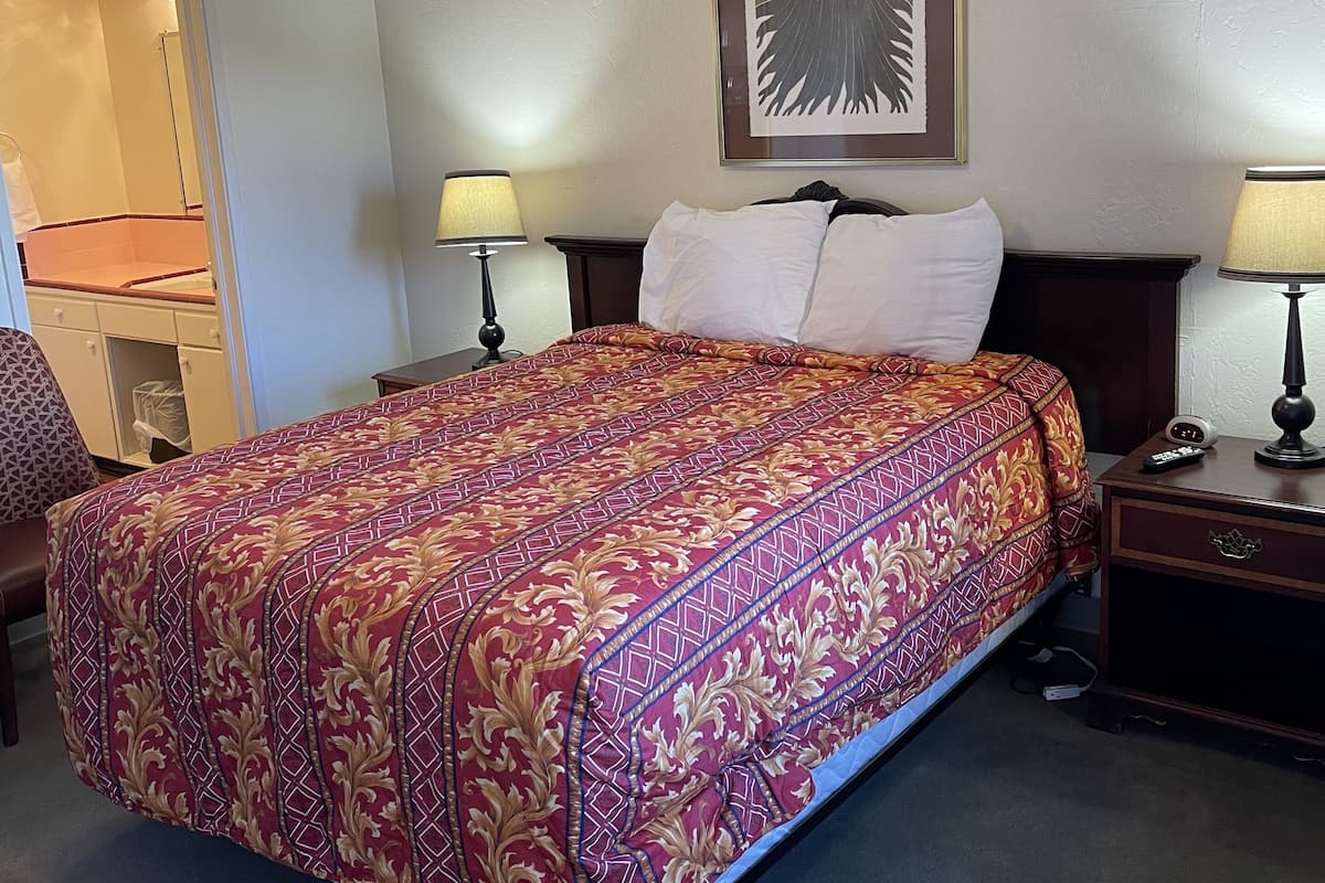 Ett hotellrum med en säng, två sänglampor, en takfläkt, ett inramat konstverk och ett nattduksbord med en fjärrkontroll.