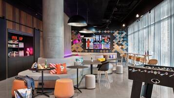 A modern lounge area with a foosball table, seating, a bar, and a large window.