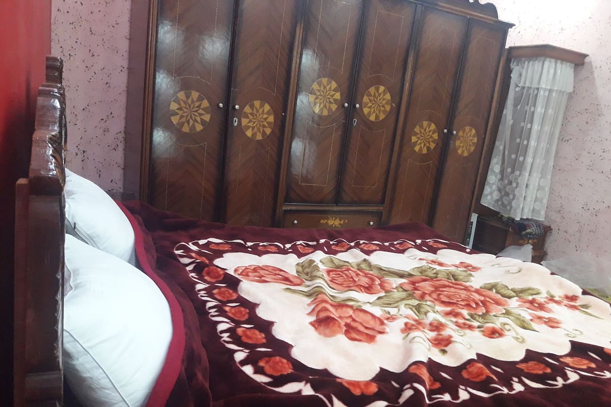 A bedroom with a bed, a wooden wardrobe, and a floral bedspread.