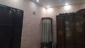 Una habitación con paredes rosadas salpicadas, un armario de madera con paneles decorativos, una ventana pequeña con cortina y un techo con iluminación empotrada.