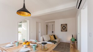 A modern kitchen with a wooden table set for breakfast, a hanging pendant light, and a view into a living area with a sofa and a painting. - Santa Justa Apartments, Downtown Center (Lisbon)