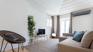 A modern living room with a sofa, a wicker chair, a TV, a plant, and a large window. - Santa Justa Apartments, Downtown Center (Lisbon)