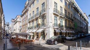 A street with outdoor seating, parked cars, and buildings with balconies and awnings. - Santa Justa Apartments, Downtown Center (Lisbon)