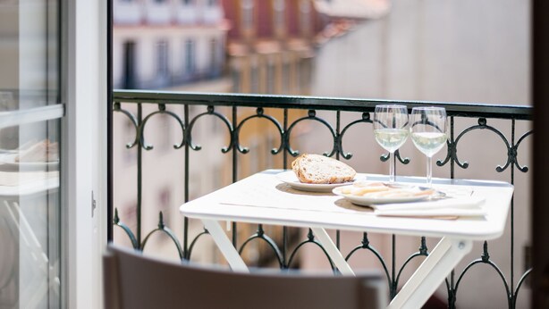 A balcony with a table set for two, featuring a plate of bread and two glasses of white wine. - Santa Justa Apartments, Downtown Center (Lisbon)